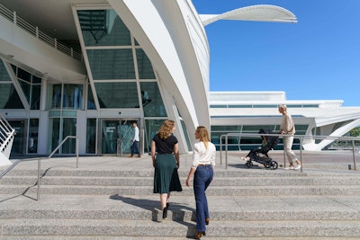 Various museum guests—a group of friends, a mother pushing a stroller, and an individual patron—approach the museum’s main entrance off Art Museum Drive.